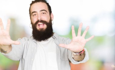Uzun saç, sakal ve gösterilen ve parmakları ile işaret küpe ile genç adam kendinden emin ve mutlu gülümseyerek süre on numara.