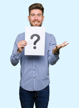 Kocaman bir gülümseme ile çığlık zaferini kutluyor ve ellerini kaldırdı soru işareti çok mutlu ve heyecanlı, kazanan ifade ile kağıt tutan genç yakışıklı adam