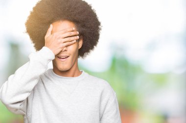 Afrikalı-Amerikalı genç afro saçlı sportif kazak gülümseyen ve gözler için sürpriz kapsayan yüz el ile gülüyor. Kör kavramı.