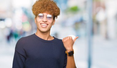 Afro seyir ve başparmak yanında yukarıyı mutlu yüz ile gülümseyen gözlüklü genç yakışıklı adamla.