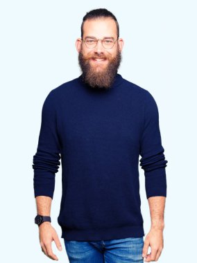 Genç sarışın adam yüzünde gözlük ve mutlu ve güzel bir gülümseme ile balıkçı yaka kazak giyiyor. Şanslı kişi.