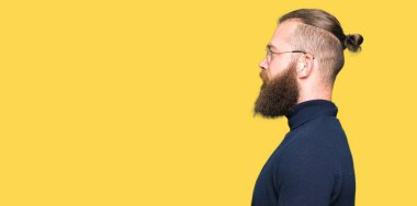 Yan arayan gözlük ve balıkçı yaka kazak giyen genç sarışın adam, güvenli bir gülümseme ile doğal yüzü ile profil poz rahatlayın.