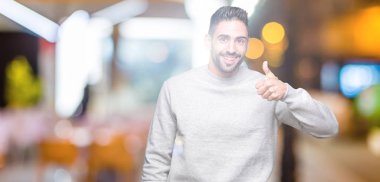 Hareketi el ile mutlu yaşasın yapıyor izole arka plan üzerinde sweatshirt giyen genç yakışıklı adam. Başarı gösteren kameraya bakarak ifade onaylama.