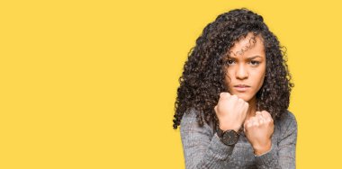 Gri kazak giyen kıvırcık saçlı Genç güzel kadın yumruk savunma jest ile savaşmak için hazır, öfkeli ve üzgün yüz, sorun korkuyor