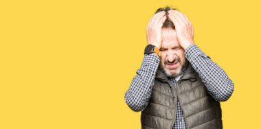 Orta yaş yakışıklı adam kış yelek giyen baş ağrısı umutsuz muzdarip ve stresli çünkü ağrı ve migren. Eller baş üstünde.