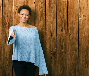 Tebrik ve konuksever dost sunan karşılıklı gülümseyen izole arka plan üzerinde bir kazak giyen genç güzel Afro-Amerikan kadın. Başarılı iş.