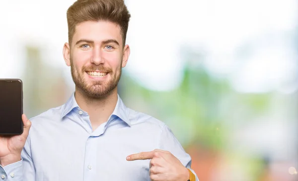 Young handsome man business showing smartphone screen with surprise face pointing finger to himself