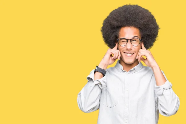 非洲青年美国人戴着戴着非洲头发的眼镜 用手指用烦躁的表情为嘈杂的音乐的噪音覆盖耳朵 聋哑人的概念 — 图库照片