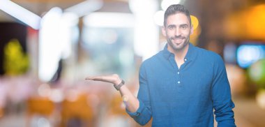 Genç yakışıklı adam neşeli sunulması ve kameraya bakarak avucunun ile işaret gülümseyen izole arka plan üzerinde.