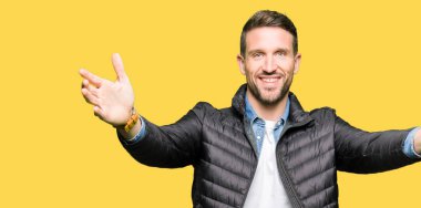 Yakışıklı adam sarılmak için Kollarını açarak gülümseyerek kameraya bakarak kış palto giyiyor. Neşeli ifade kucaklayan mutluluk.