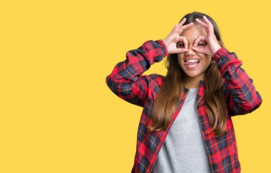 Dilini, parmaklarının arasından baktığını yapışmasını dürbün gibi ok jest yapıyor izole arka plan üzerinde bir ceket giyen genç güzel esmer kadın. Deli ifade.