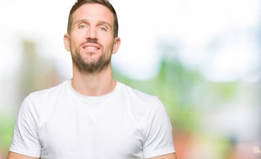 Yakışıklı adamın Casual beyaz t-shirt eller birlikte giydiğini ve parmakları rahat ve neşeli gülümseyen geçti. Başarı ve iyimser