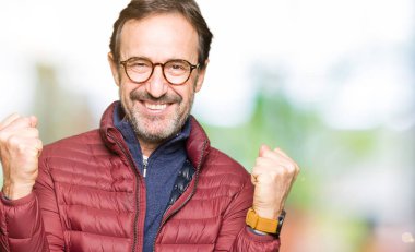 Orta yaş yakışıklı adamın gözlük ve kış ceket kutluyor giydiğini şaşırttı ve başarı için kaldırdı Kollarını açarak hayret ve gözleri açık. Kazanan kavramı.