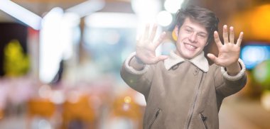 Gösterilen arka plan üzerinde kış ceket giyen genç yakışıklı adam izole ve parmakları ile işaret numara 9 kendinden emin ve mutlu gülümseyerek süre.