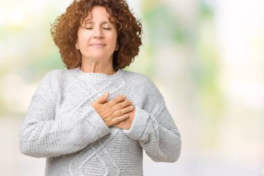 Göğüs kapalı gözlerle ellerinde ve yüzünde minnettar jest ile gülümseyen izole arka plan üzerinde kış kazak giyen güzel orta ager üst düzey kadın. Sağlık kavramı.