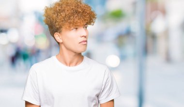 Afro saçlı görünümlü yan ve dik dik bakma uzağa düşünce gülümseyen casual beyaz t-shirt giyen genç yakışıklı adam.