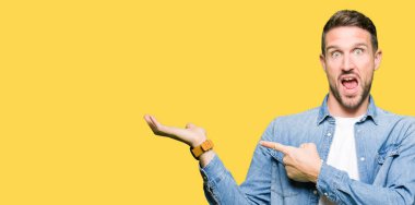 Mavi gözlü ve sakal giyen kot ceket ile yakışıklı adam hayran ve kamera gülümseyen el ile sunmak ve parmak ile işaret ederken.