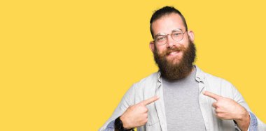 Yüzünde gülümseme ile kendine güvenen görünümlü gözlük takan genç sarışın adam, parmaklarıyla gurur ve mutlu kendini işaret.