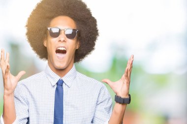 Afro saçlı Genç Afrikalı Amerikan iş adamı güneş gözlüğü deli ve deli bağırarak ve agresif ifade ve kollar ile bağırarak kaldırdı. Hayal kırıklığı kavramı.