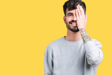 El yüz ve sürpriz duygu kendinden emin gülümseme ile tek gözüyle kapsayan izole arka plan üzerinde sweatshirt giyen genç yakışıklı adam.