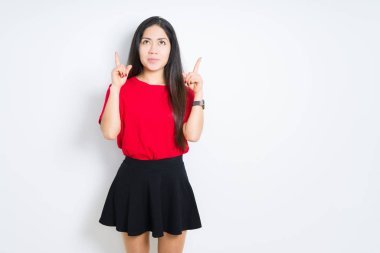İzole arka plan üzerinde kırmızı t-shirt ve etek giyen güzel esmer kadın şaşırttı ve yukarı bakarak ve parmakları ile işaret ve kolları kaldırdı şaşırttı.