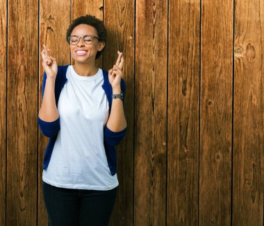 Umut ve gözleri kapalı geçiş parmaklarıyla gülümseyen izole arka plan üzerinde gözlük takan genç güzel Afrikalı-Amerikalı kadın. Şans ve batıl kavramı.