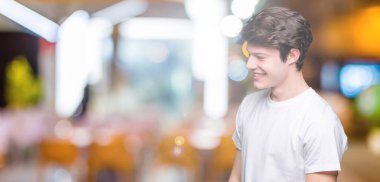 Uzak tarafına yüzünde, doğal ifade gülümseme ile seyir izole arka plan üzerinde rahat beyaz t-shirt giyen genç yakışıklı adam. Kendine güvenen gülüyor.