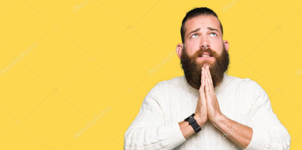 Young hipster man wearing winter sweater begging and praying with hands together with hope expression on face very emotional and worried. Asking for forgiveness. Religion concept.