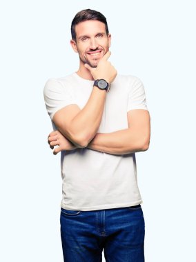 Yakışıklı adam emin çapraz kollar ve çeneme kaldırdı el ile gülümseme ile kameraya bakarak casual beyaz t-shirt giyiyor. Pozitif düşünce.