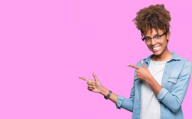 Güzel genç Afro-Amerikan kadın gülümseyerek ve iki elleri ve parmakları ile tarafına işaret kamera bakarak izole arka plan üzerinde gözlük.