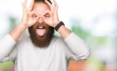 Rahat kazak giyen genç sarışın adam dürbün yapışması gibi ok jest yapıyor, gözleri parmaklarla bakıyor. Çılgın ifade.