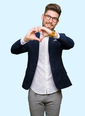 Kalp simgesi ve elleriyle şekil gösterilen aşık gülümseyen gözlüklü genç yakışıklı iş adamı. Romantik kavramı.