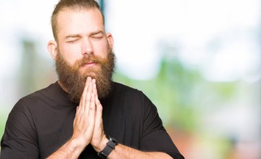 Yalvarıyor ve umut ifade yüzünde çok duygusal ve endişe ile birlikte elleriyle dua rahat t-shirt giyen genç sarışın adam. Bağışlanmak. Din kavramı.