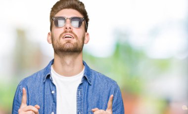 Kot ceket giyen genç yakışıklı zarif adam hayran ve bakmak ve parmaklar ve yükseltilmiş kollar ile işaret şaşırttı.