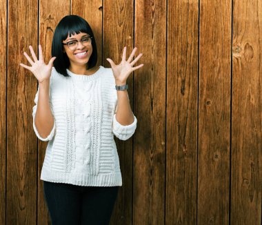 Güzel genç Afro-Amerikan kadın gözlük gösterilen ve parmakları ile işaret izole arka plan üzerinde number ten kendinden emin ve mutlu gülümseyerek süre.