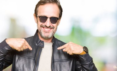 Güneş gözlüğü ve yüzünde gülümseme ile kendinden emin görünüyorsun, kendini gururlu ve mutlu parmakları ile işaret siyah deri ceket giyen orta yaş yakışıklı adam.