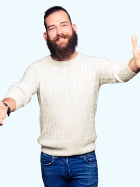 Sarılmak için kollarını açarak gülümseyerek kameraya bakarak kış kazak giyen genç hipster adam. Neşeli ifade kucaklayan mutluluk.