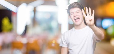 Yakışıklı delikanlı gösterilen ve parmakları ile işaret izole arka plan üzerinde rahat beyaz t-shirt giyen süre kendinden emin ve mutlu gülümseyerek dört numara.