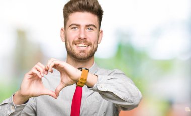 Kalp simgesi ve elleriyle şekil gösterilen aşık gülümseyen genç yakışıklı iş adamı. Romantik kavramı.