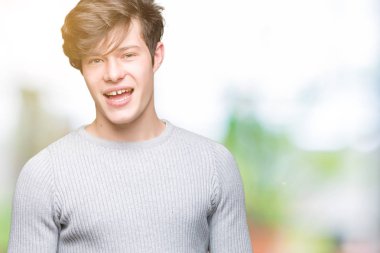 Seksi bir ifadeyle, neşeli ve mutlu yüzünü kameraya bakarak göz kırpıyor izole arka plan üzerinde kış kazak giyen genç yakışıklı adam.