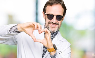 Yakışıklı orta yaş Doktor adam aşık kalp simgesi ve elleriyle şekil gösteren gülümseyen güneş gözlüğü takıyor. Romantik kavramı.