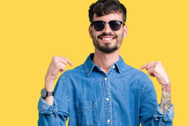 Yakışıklı delikanlı yüzünde gülümseme ile kendinden emin görünüyorsun, kendini gururlu ve mutlu parmakları ile işaret izole arka plan üzerinde güneş gözlüğü takıyor.