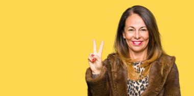 Güzel orta yaş zarif kadın, zafer işareti yaparken kamera mutlu yüz göz kırpıyor ile gülümseyen vizon ceket giyiyor. İki numara.