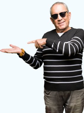 Kış kazak ve hayrete ve el ile sunulması ve parmak ile işaret ederken kameraya gülümseyen güneş gözlüğü takan yakışıklı komuta sizde.