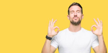 Casual beyaz t-shirt dinlenmek giydiği ve gözleri ile gülümseyen yakışıklı adam parmak ile meditasyon jest yapıyor kapalı. Yoga kavramı.