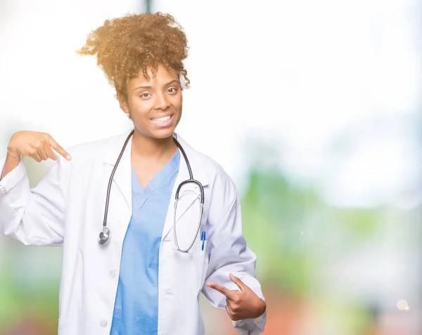 Young african american doctor woman over isolated background looking confident with smile on face, pointing oneself with fingers proud and happy.