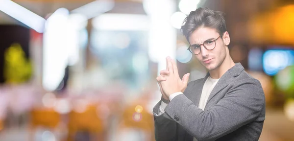 Young business man wearing glasses over isolated background Holding symbolic gun with hand gesture, playing killing shooting weapons, angry face