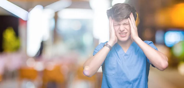 年轻的医生穿着医疗制服在孤立的背景下遭受头痛绝望和压力 因为疼痛和偏头痛 双手放在头上 — 图库照片