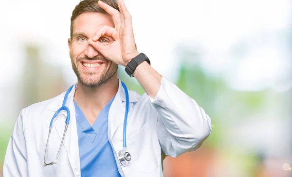 幸せそうな顔で指を通して見る目の手で のジェスチャーを行う分離の背景に医療制服を着てハンサムな医者の男 — ストック写真