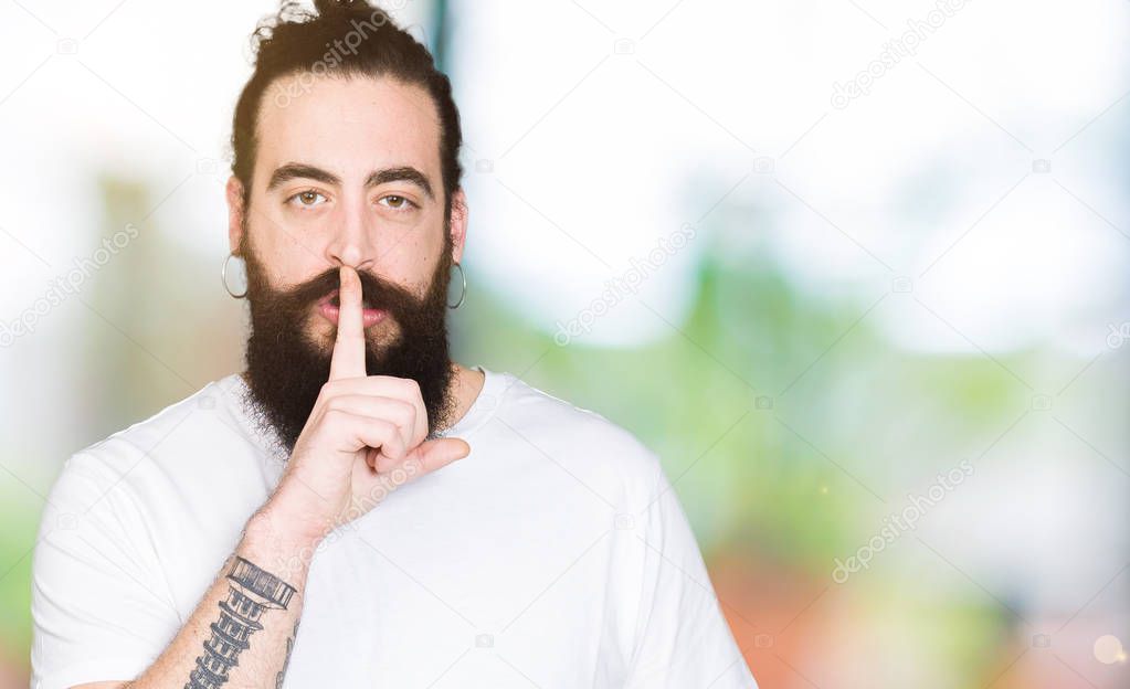 Young hipster man with long hair and beard wearing casual white t-shirt asking to be quiet with finger on lips. Silence and secret concept.